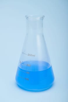 Still life with graduated flat bottomed lab flask with blue liquid solution, isolated over blue color background. Chemistry. Science, Clinical research. Healthcare and medicine concept. Vertical shot