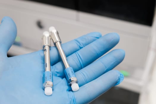 Small HPLC 50 mm columns for separation compounds in laboratory worker hand in rubber glove. Fast high performance liquid chromatography analysis in chemical and microbiological laboratory. Clinical, toxicological and forensic analysis.