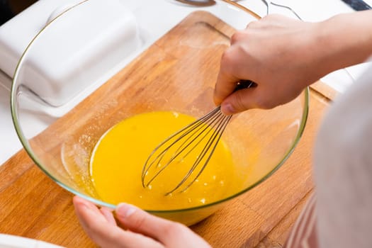 Close up of a womans hands whipping eggs for making dough on the wooden desk in the kitchen. Homemade cooking.
