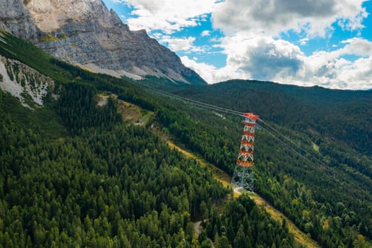 High voltage electric transmission tower in the mountains surrounded by trees, aerial view