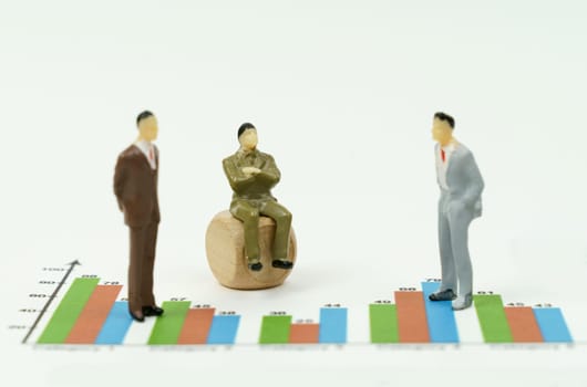 Business concept. On the financial charts there are miniature figures of businessmen, one is sitting on a cube. Business - conversation