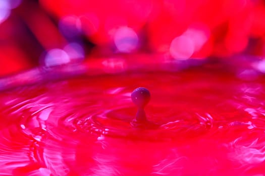 A drop falls into a dense liquid with a red background. Abstract colorful background