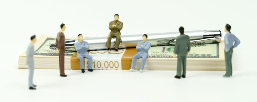 Business and finance concept. On a white surface lies a pack of dollars, on which there are a pen and miniature figures of people. Corporate meeting.