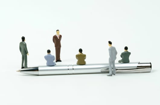 Business and finance concept. On a white surface are miniature figures of businessmen - holding a meeting, a seminar. Some businessmen are sitting on the handle, others are standing.