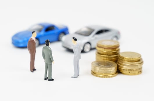 Car business. Three miniature figures of a businessman, coins and cars in the background.