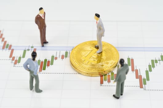 Cryptocurrency and business concept. On the business charts are bitcoins and miniature figures of people.