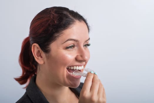 Close-up of a woman putting on transparent plastic retainers. The girl uses a device to straighten her teeth.