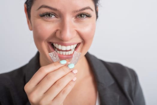 Close-up of a woman putting on transparent plastic retainers. The girl uses a device to straighten her teeth.