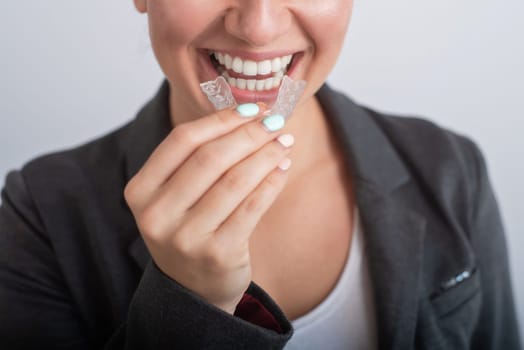 Close-up of a woman putting on transparent plastic retainers. The girl uses a device to straighten her teeth.