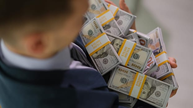 Businessman carrying many bundles of dollar bills closeup. Money transactions and profit growth in business concept