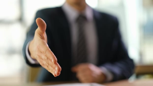 Businessman holding out his hand for handshake at work in office closeup. Business meeting concept