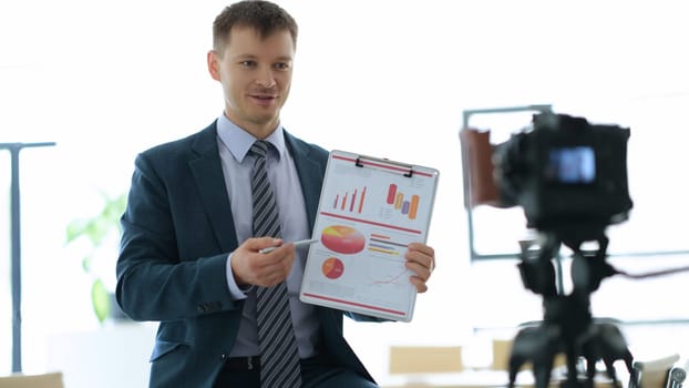 Business coach blogger showing graphs on documents in front of camera in office. Business webinars and seminars online concept