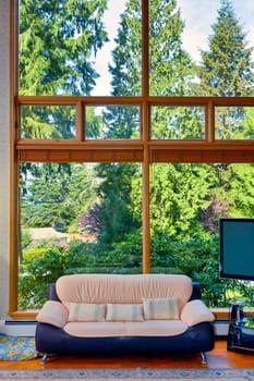 Warm wooden interior of beautiful living room in luxury house. Leather couch and TV set in front of huge window in living room.