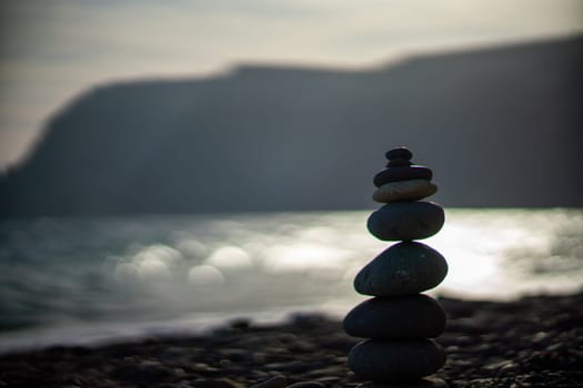 Pebble pyramid silhouette on the beach. Sunset with sea in the background. Zen stones on the sea beach concept, tranquility, balance. Selective focus.