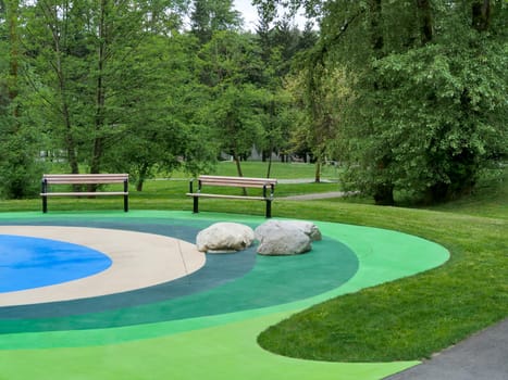 Recreational area in a park with two benches on colored ground surface with big rocks beside.