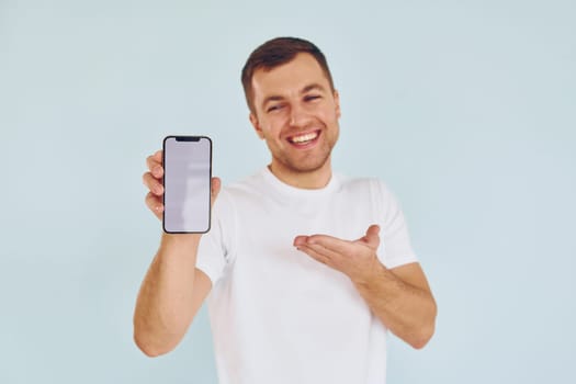 Man in casual clothes standing in the studio with phone in hands.