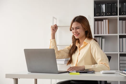 Success at work, good deal. Asian business woman looks at the laptop screen, screams excitedly and raises his fists in a victory gesture.