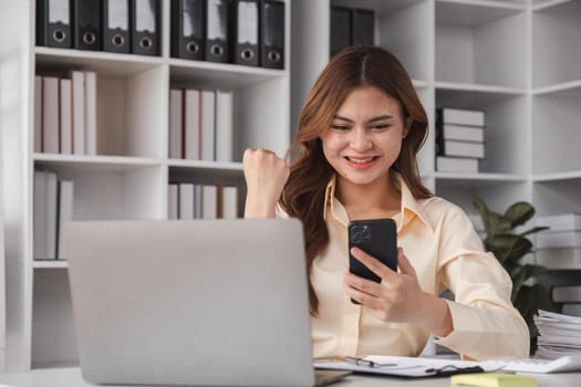 Success at work, good deal. Asian business woman looks at the laptop screen, screams excitedly and raises his fists in a victory gesture.