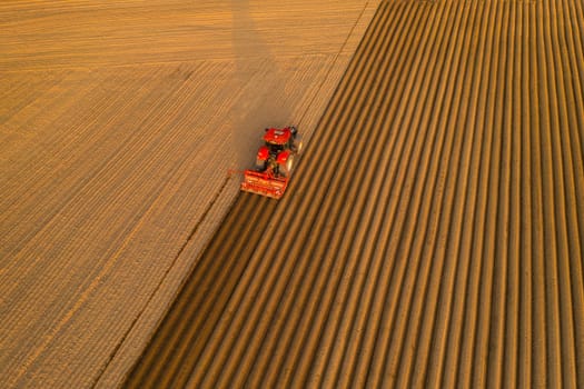 PRAGUE , CZECH REPUBLIC - MARCH 18 2022: Tractor drives across field leaving long straight furrows behind. Contemporary agricultural machine helps in countryside aerial view