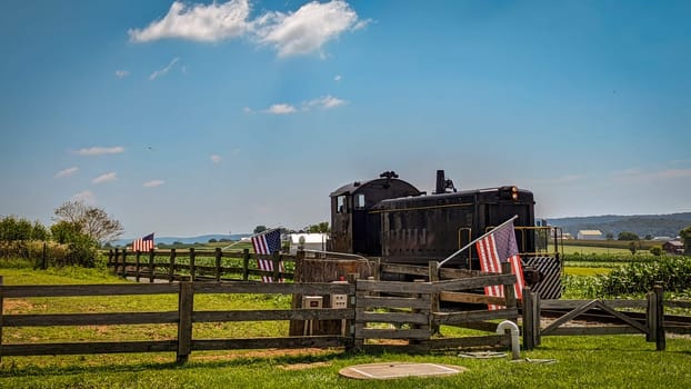 A Restored Diesel Locomotive Approaches a Fence With Gently Waving American Flags on It On a Sunny Summer Day