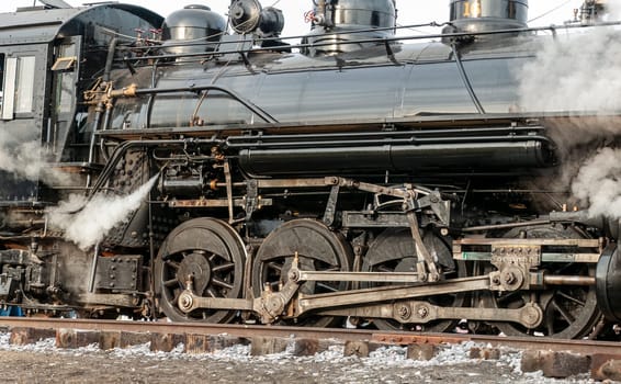 A Close Up of a Steam Trains Running Drive Gear as it Passes with Steam Blowing Out