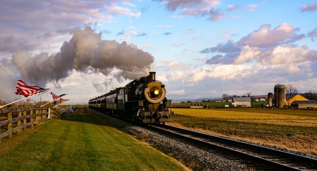 A View of a Classic Steam Passenger Train Approaching, With American Flags Attached to a Fence on a Sunny Autumn Day