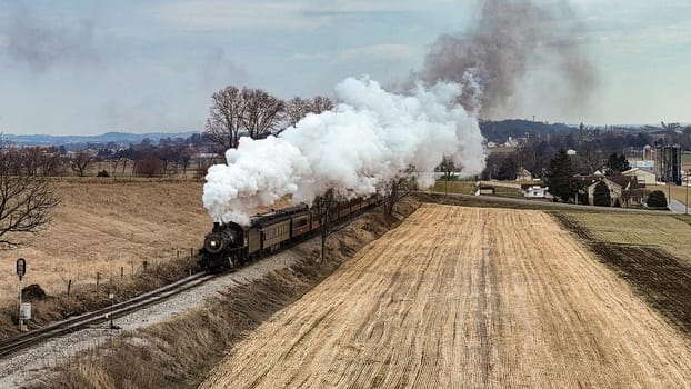 A Drone View of a Steam Locomotive Approaching Traveling Thru Fields and Meadows, Blowing White Smoke on a Winter Day