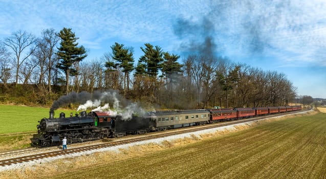 A Side Aerial View of a Steam Engine Waiting, all Steamed Up, While the Engineer Checks and Oils the Engine, While it is Blowing Smoke on a Winter Day