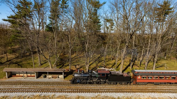 A Drone View of a Restored Steam Passenger Train Traveling Thru Farmlands Pulling Up to a Small Station on an Autumn Day