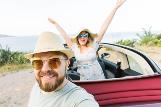 Happy beautiful couple in love taking a selfie portrait driving a convertible car on the road at vacation. Rental cars and vacation concept