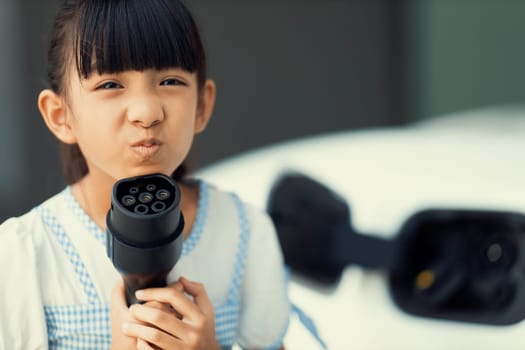 A playful girl holding and pointing an EV plug, a home charging station providing a sustainable power source for electric vehicles. Concept of progressive new generation with ecological awareness.