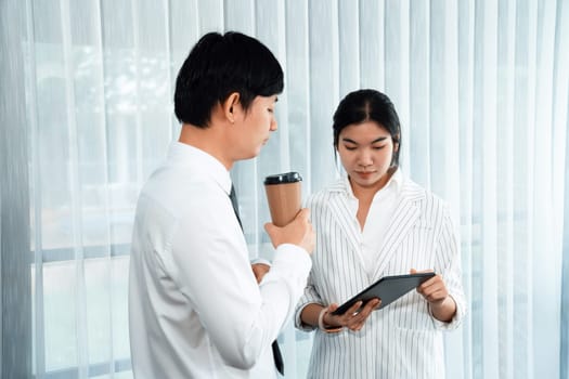 Manager advising guiding younger colleague with tablet in workplace. Couple businesspeople in formal wear working together on financial strategy as concept of teamwork and harmony in office.