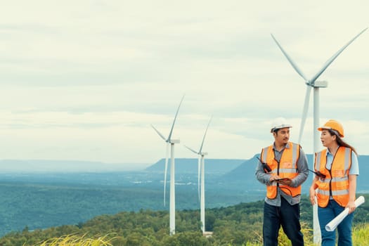 Male and female engineers working on a wind farm atop a hill or mountain in the rural. Progressive ideal for the future production of renewable, sustainable energy.