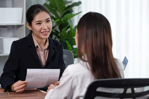 Two asian women conduct job interview in office. Applicants wear formal suit while talking about her CV and job application. Interviewer ask inquiry in positive and conversational manner. Enthusiastic