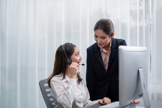 Asian female customer support operator wearing headset is guided by her supportive manager. Experienced colleague help operator handle a call with a client, providing advice and guidance. Enthusiastic