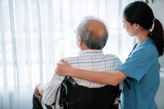 Rear view of a caregiver and her contented senior patient gazing out through the window. Elderly illness, nursing homes for the elderly, and pensioner life