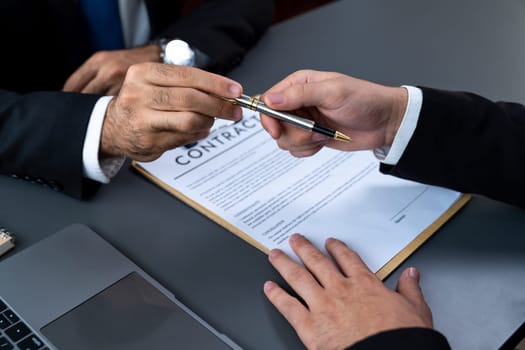 Two businesspeople sit across the desk as business deal is taking place. Corporate attorney giving a pen for client or partner to sign contract paper, sealing the deal with signature. Fervent