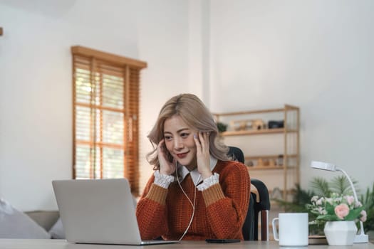 Relaxed woman listening to music with headphones pass laptop at home.