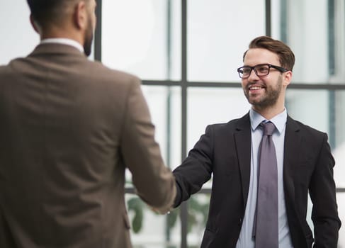 smiling businessmen shaking hands starting teamwork partnership standing in corporate work space hallway