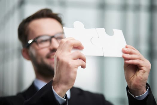 Portrait of an optimistic businessman holding puzzle pieces, solving problems, looking at the camera, wearing a black suit.
