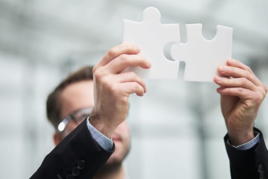 Portrait of an optimistic businessman holding puzzle pieces, solving problems, looking at the camera, wearing a black suit.