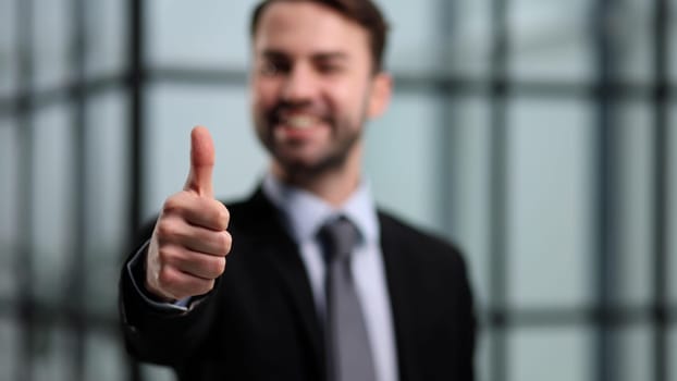 Business man or lawyer giving thumbs up in modern office building. Happy businessman showing satisfied and supportive hand gesture.