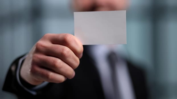 business man holding empty white business card in modern office building. Free blank copy space.