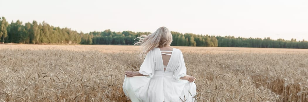 A blonde woman in a long white dress walks in a wheat field. The concept of a wedding and walking in nature.