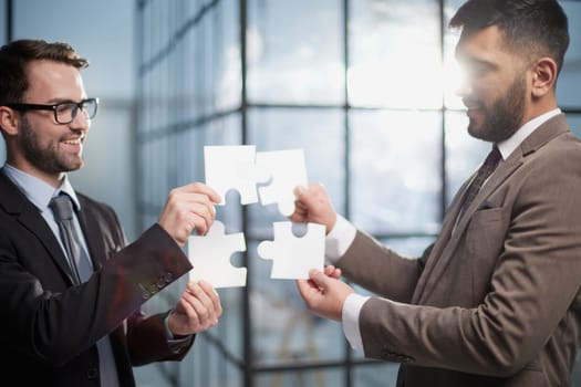 two businessmen put together a puzzle opposite each other on the background of the office