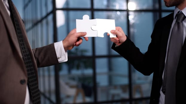 Close-up of business partners putting together two white puzzle pieces against the backdrop of an office building
