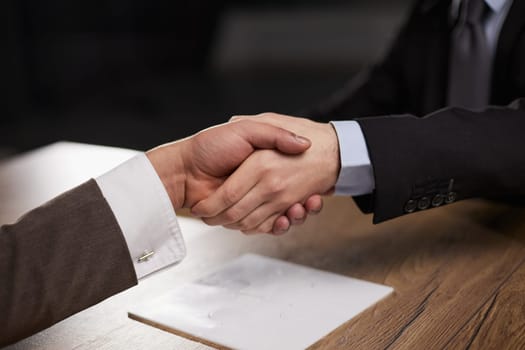 Closeup of hands of two young and successful male business people shaking hands over wooden table