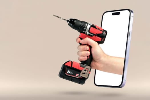 Buying power tools online. Online shopping banner. A screwdriver in hand protrudes from a mobile phone as a concept for buying tools on the Internet