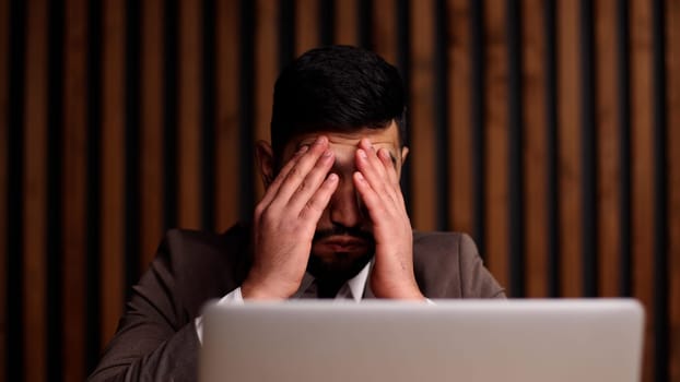 Tired man behind a computer screen from boring routine work in the office.