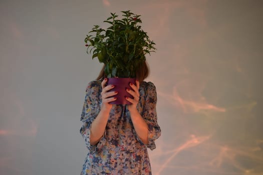 Beautiful girl with a dark face hiding behind a vase of flowers, on a white background.